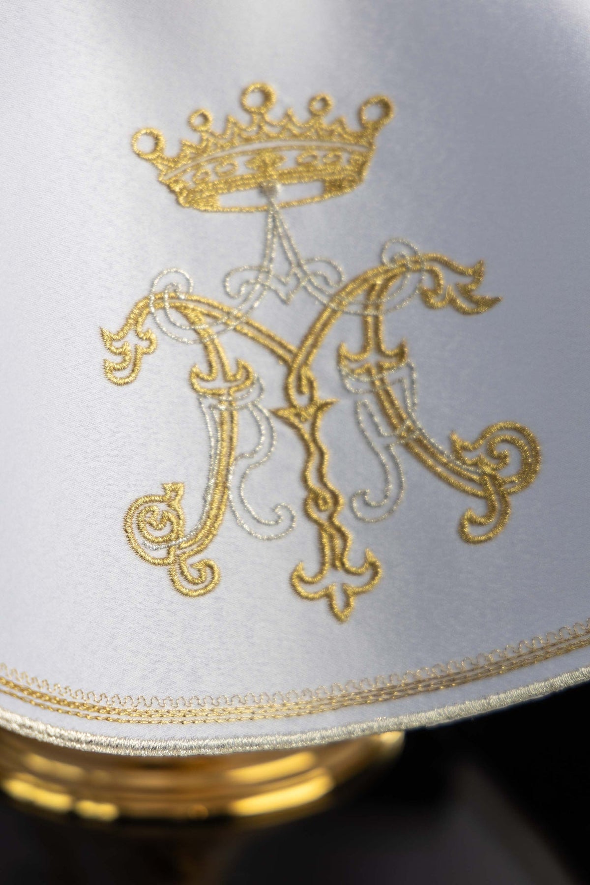 Cubrecopón con bordado mariano dorado, detalle del monograma mariano y ribete